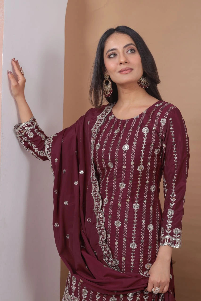 Woman wearing a maroon embroidered outfit against a beige background