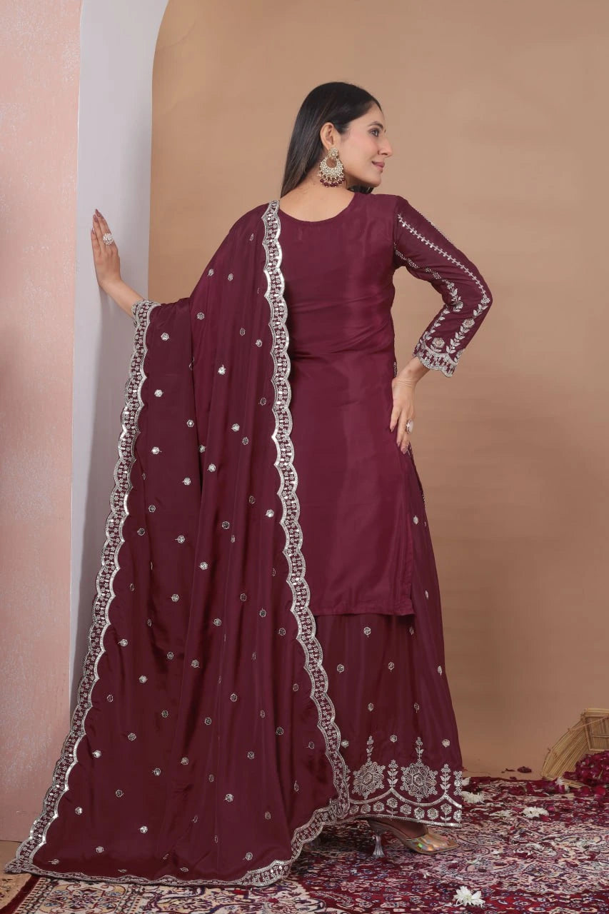 Woman in a maroon traditional outfit with a matching dupatta against a beige wall.