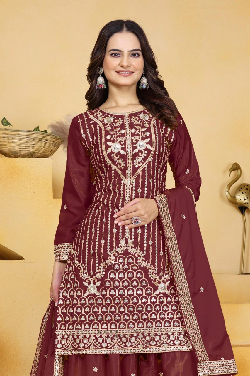 Woman wearing a maroon embroidered traditional outfit with a beige background