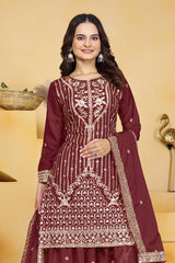 Woman wearing a maroon embroidered traditional outfit with a beige background