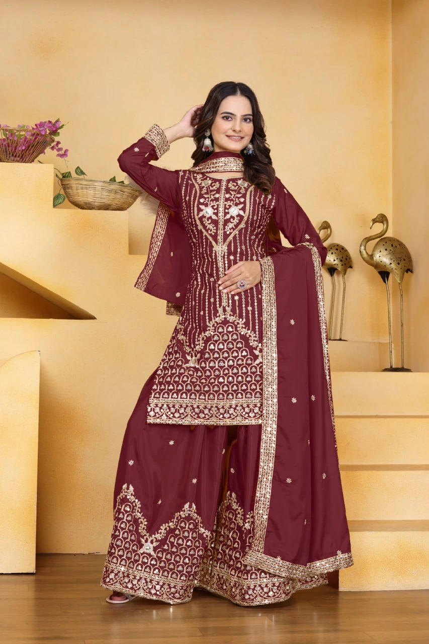 Woman wearing a maroon embroidered traditional outfit in a decorative setting.