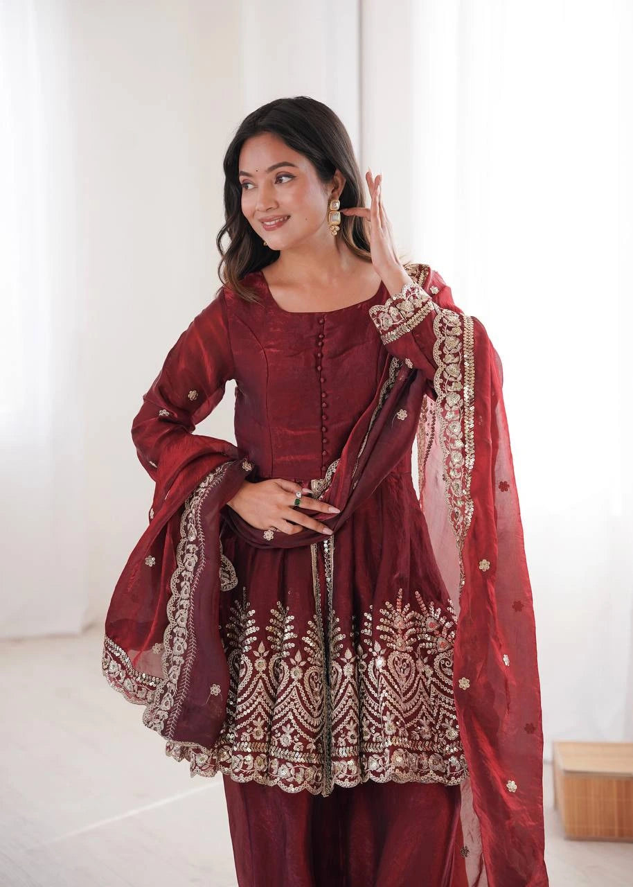 Woman wearing a maroon traditional outfit with gold embroidery against a white background