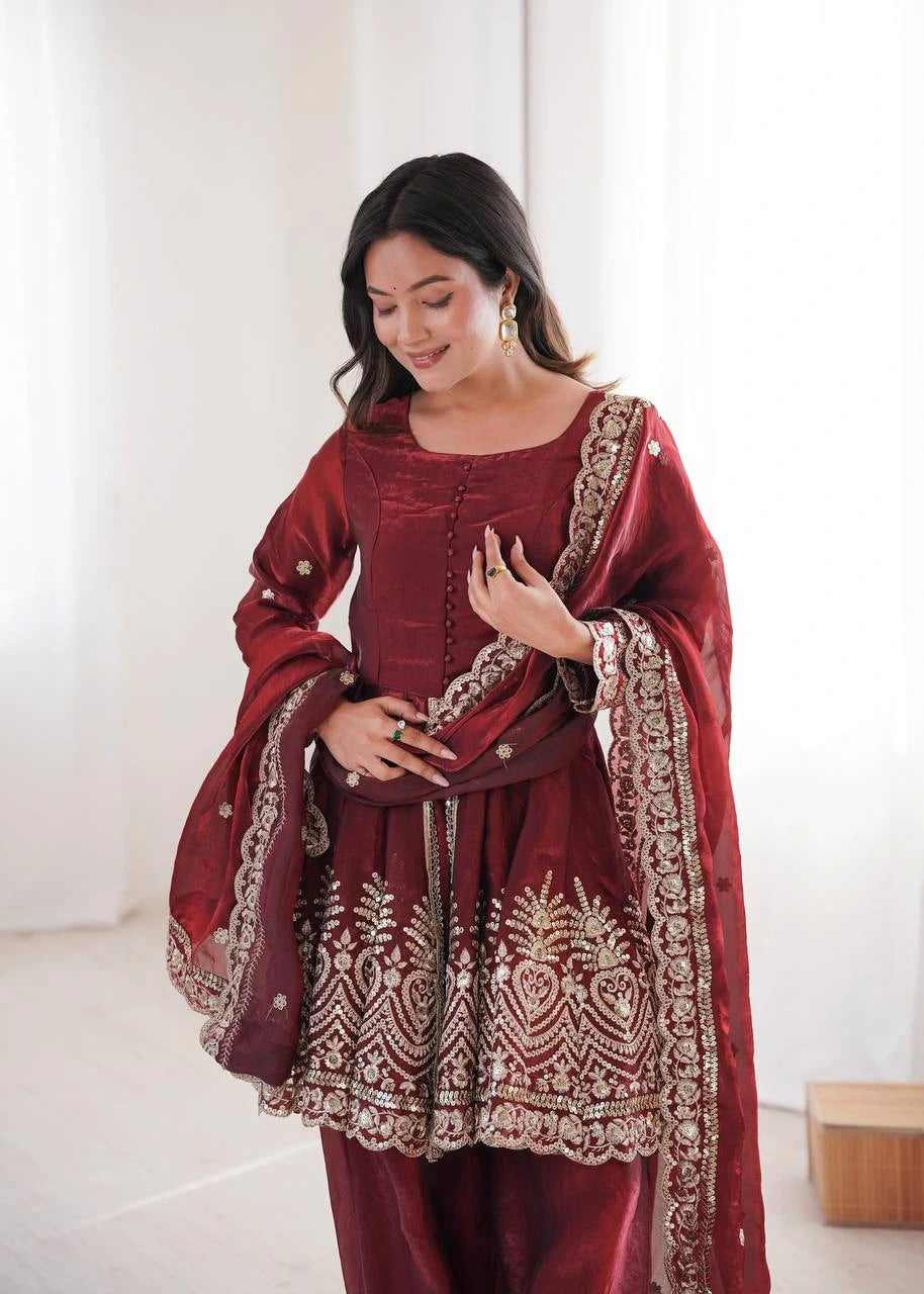 Woman wearing a maroon traditional outfit with gold embroidery in a minimalistic setting