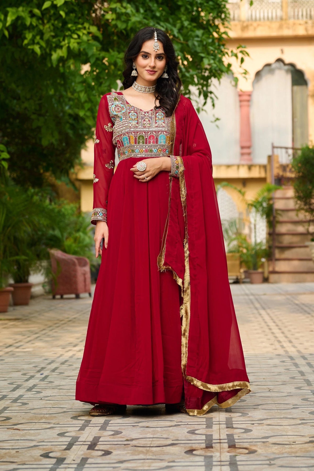 Woman in a red traditional outfit with embroidery standing outdoors.