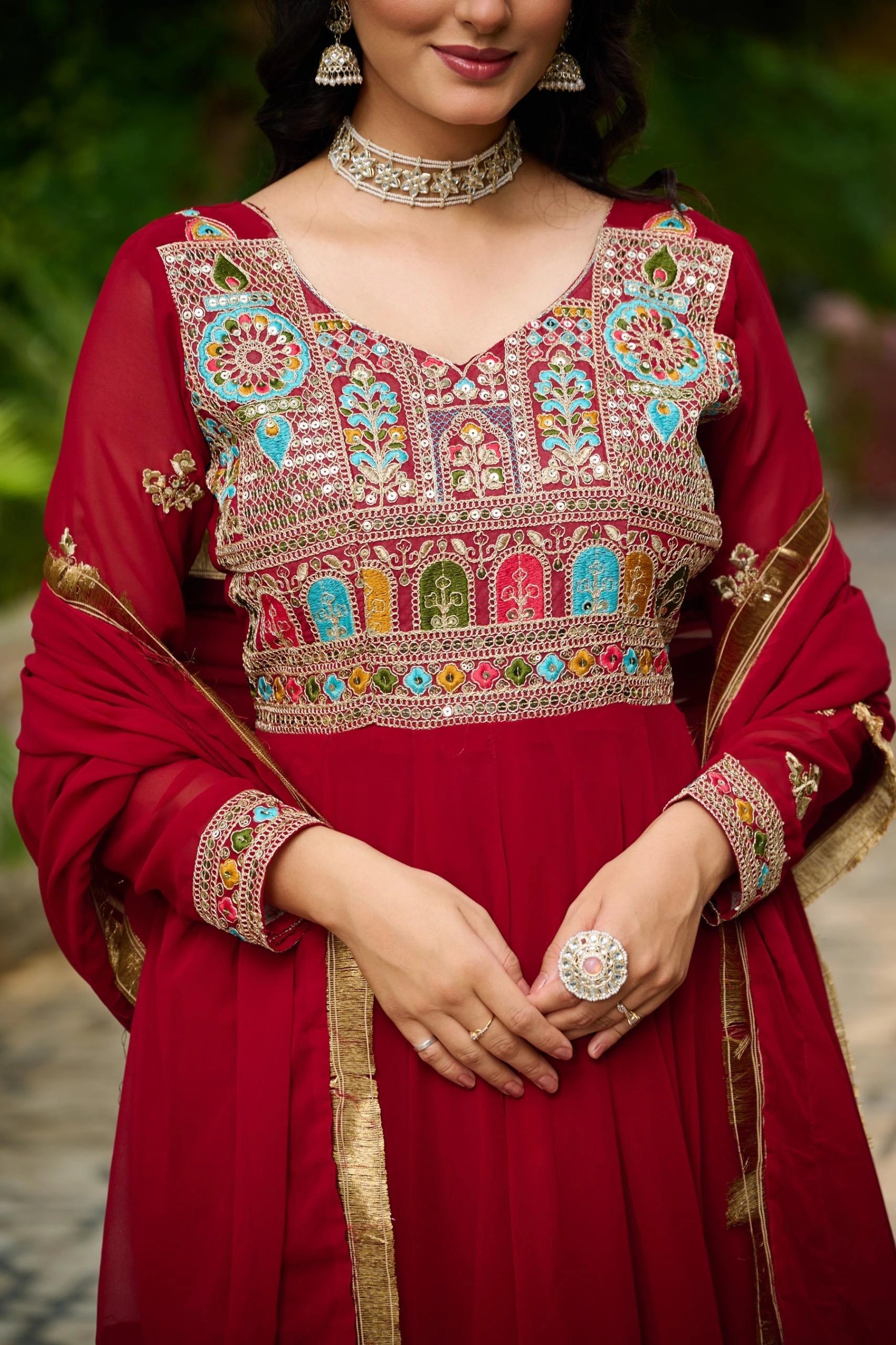 Red traditional outfit with colorful embroidery and jewelry against a blurred natural background