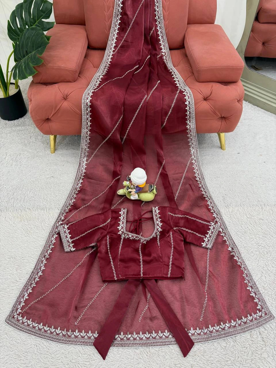 Red saree with silver border on a white floor, with a pink sofa and plant in the background.