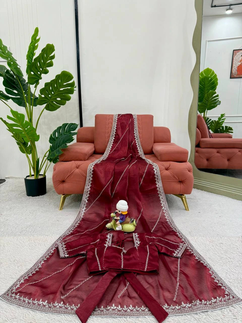 Maroon saree with white border on a white floor with red sofa and green plants in the background