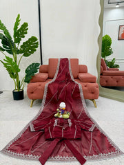 Maroon saree with white border on a white floor with red sofa and green plants in the background
