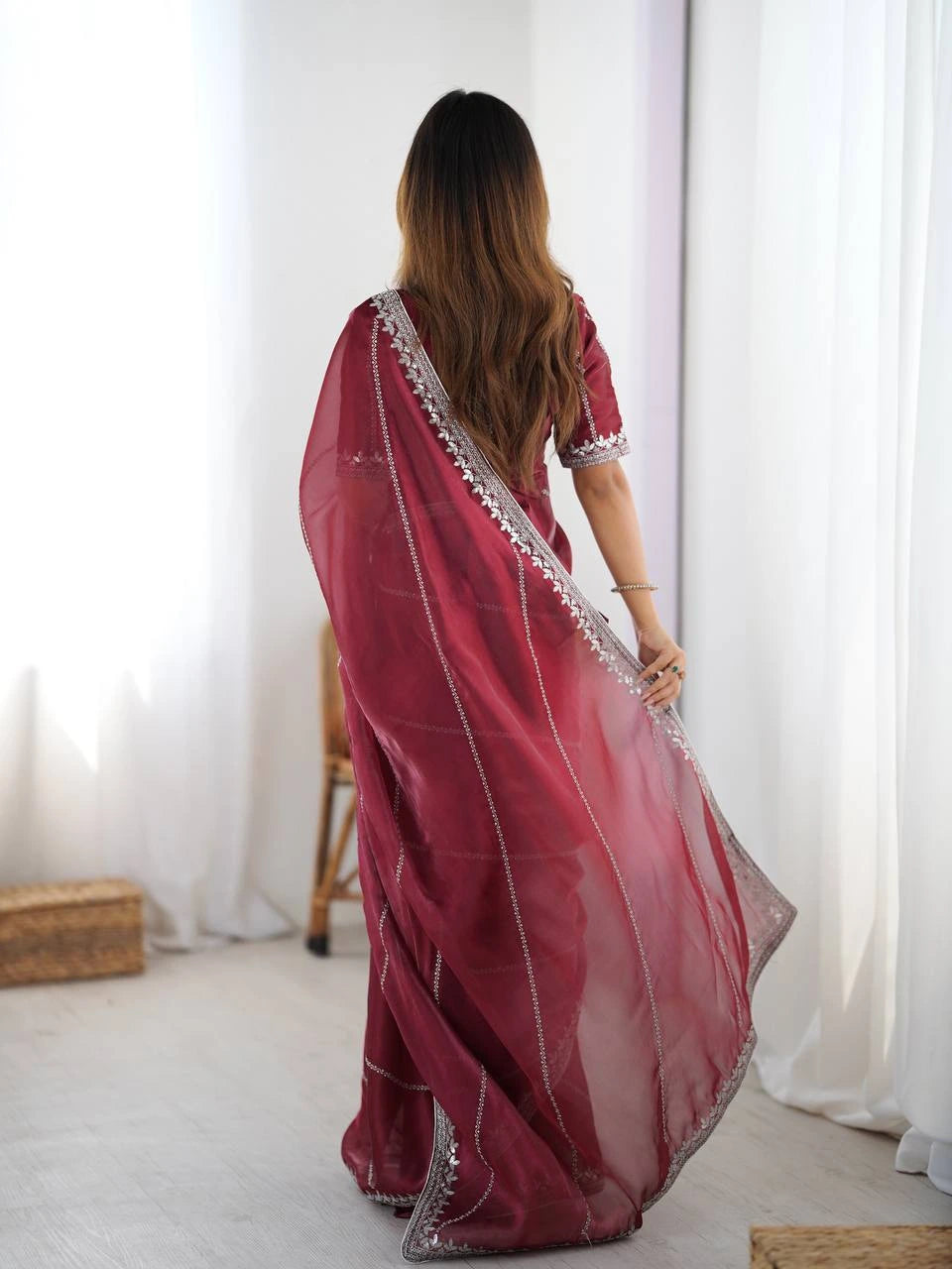 Woman wearing a red saree with white patterns in a minimal indoor setting