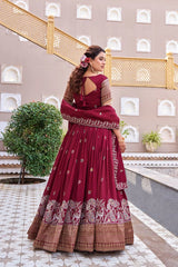 Woman in a maroon traditional outfit with intricate patterns standing in an outdoor setting.