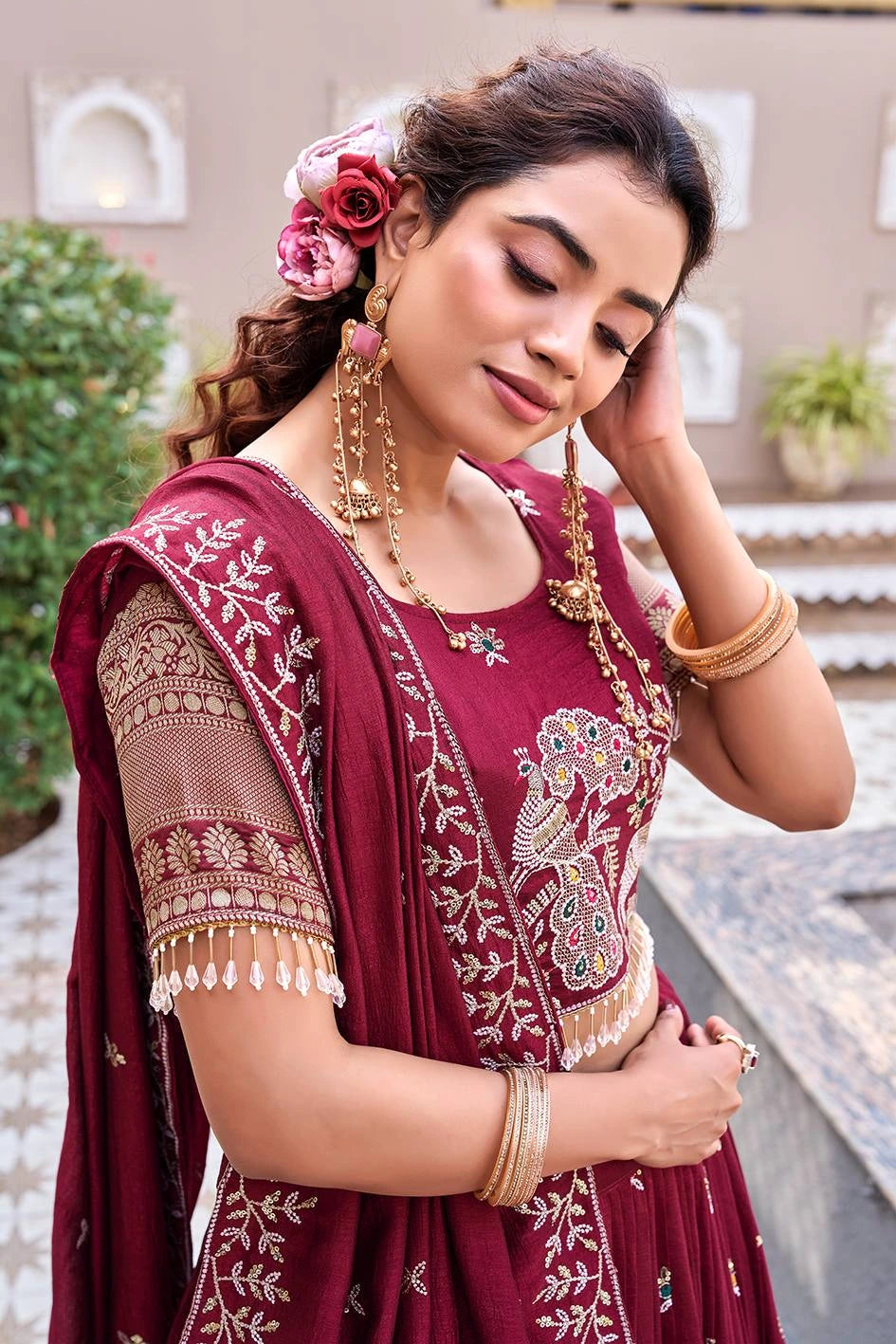 Woman in a maroon saree with gold embroidery, posing outdoors.