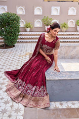 Woman in a maroon saree with gold patterns sitting on a stone ledge.