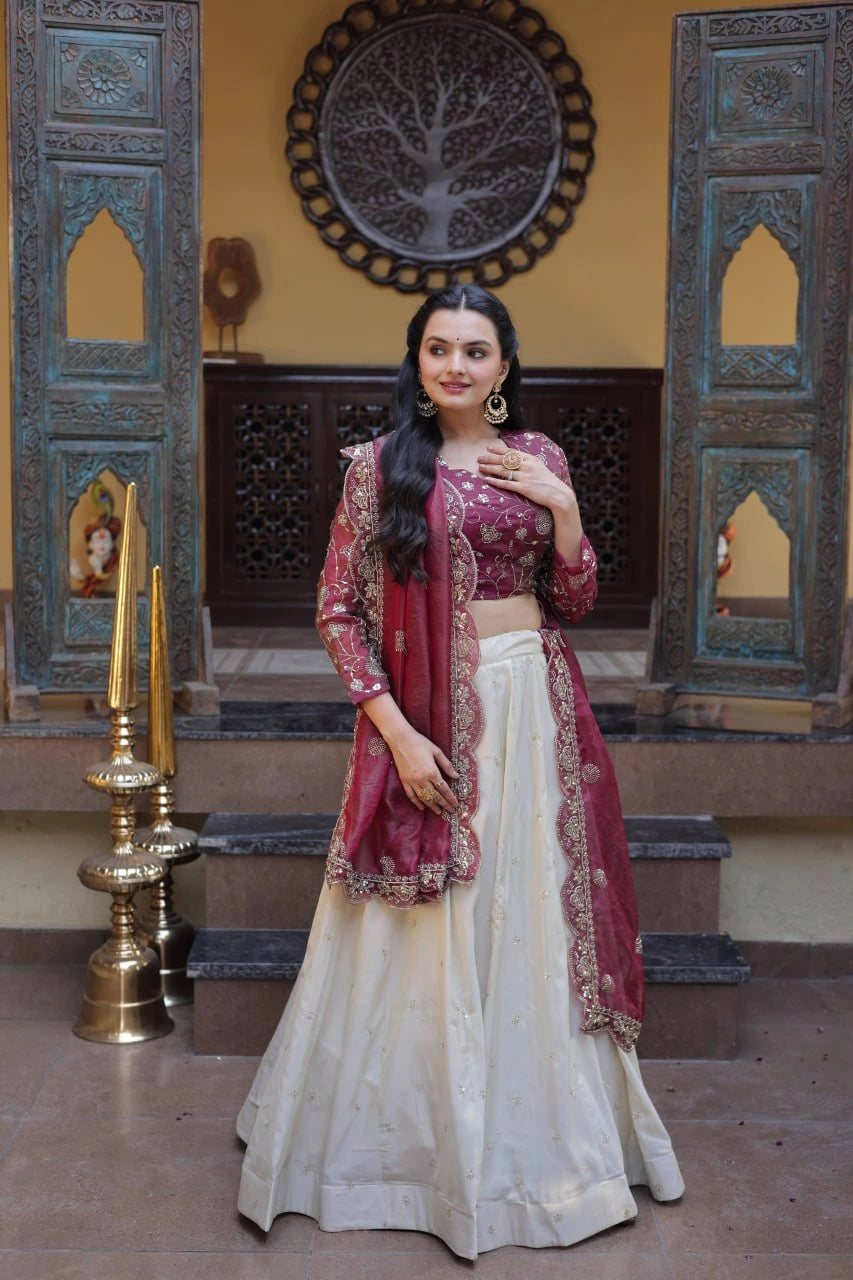 Woman in a traditional maroon and white outfit standing in an ornate interior setting.
