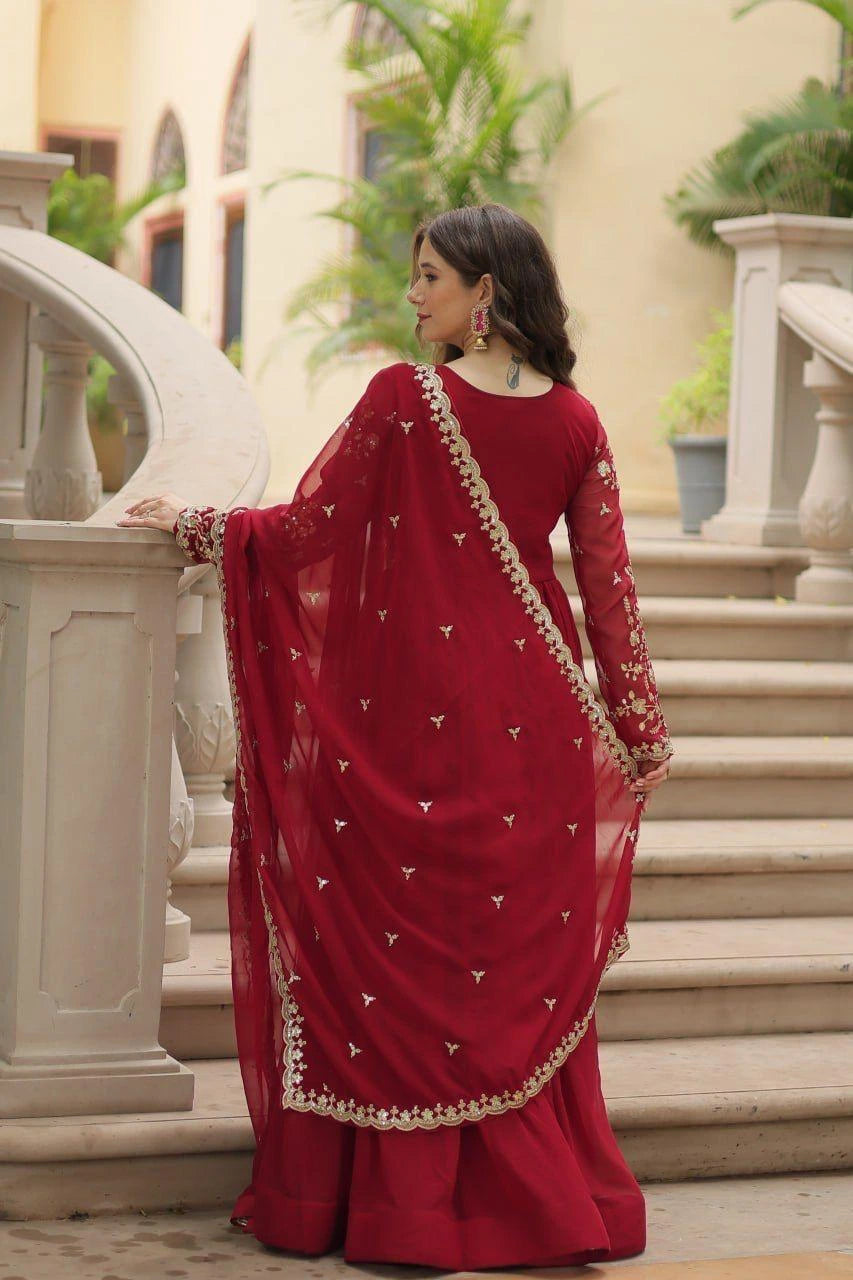 Woman in a red saree with gold details standing outdoors.