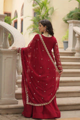 Woman in a red saree with gold details standing outdoors.
