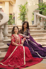 Two women in traditional red and purple dresses sitting on steps outdoors.