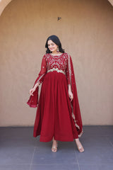Woman wearing a red traditional outfit with gold details against a beige wall.