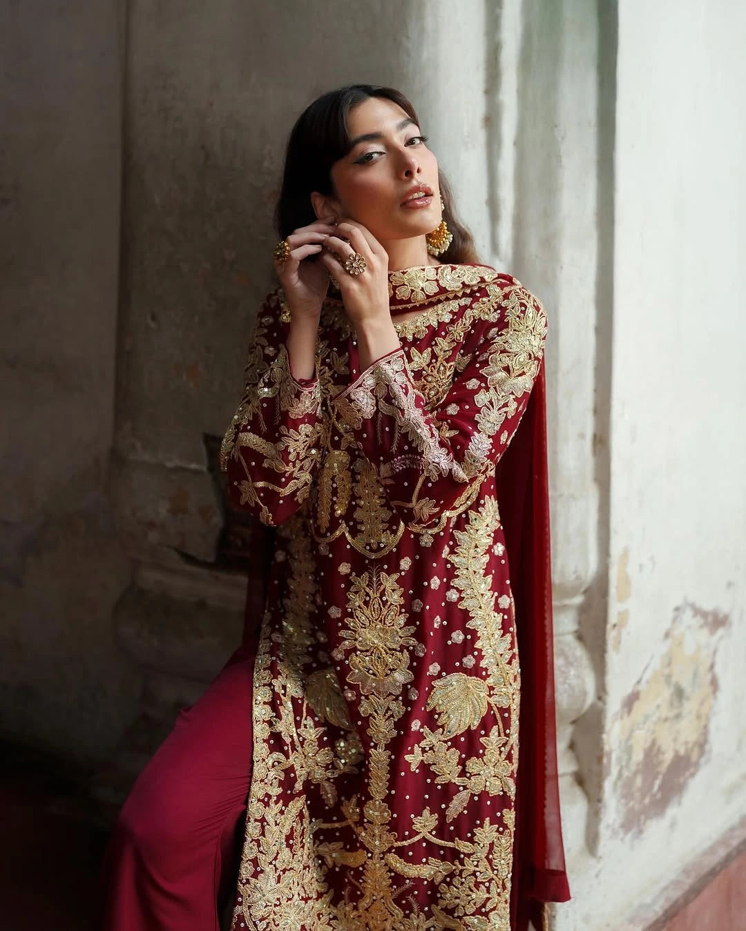 Woman wearing a red and gold embroidered traditional outfit in a softly lit room.