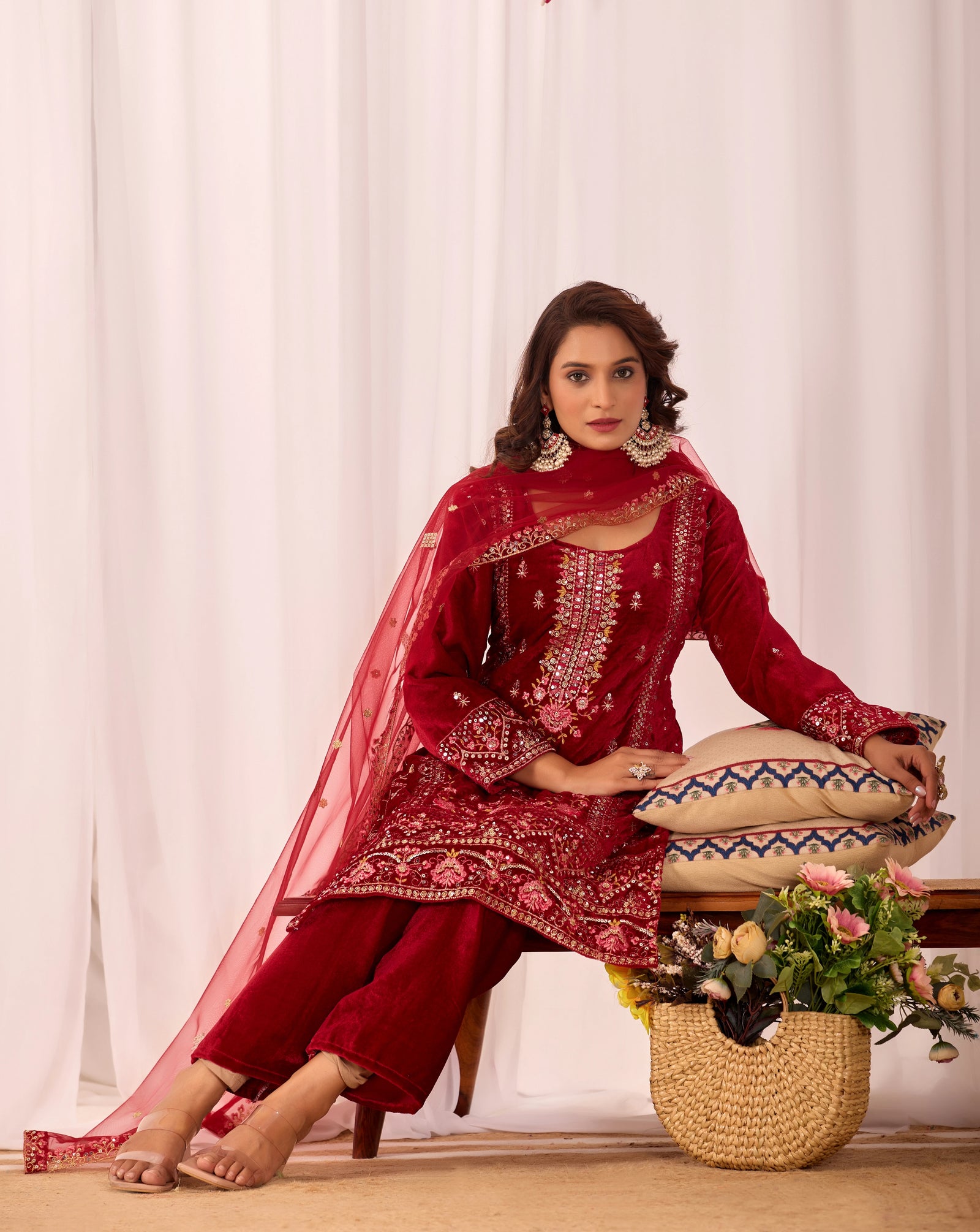 Woman in a red traditional outfit sitting on a stool with a white curtain background