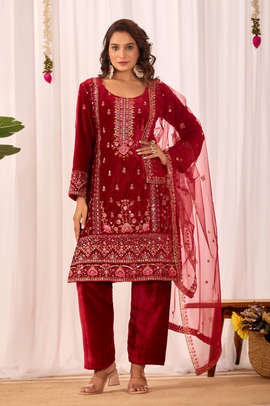 Woman wearing a red embroidered traditional outfit with a dupatta against a white curtain background