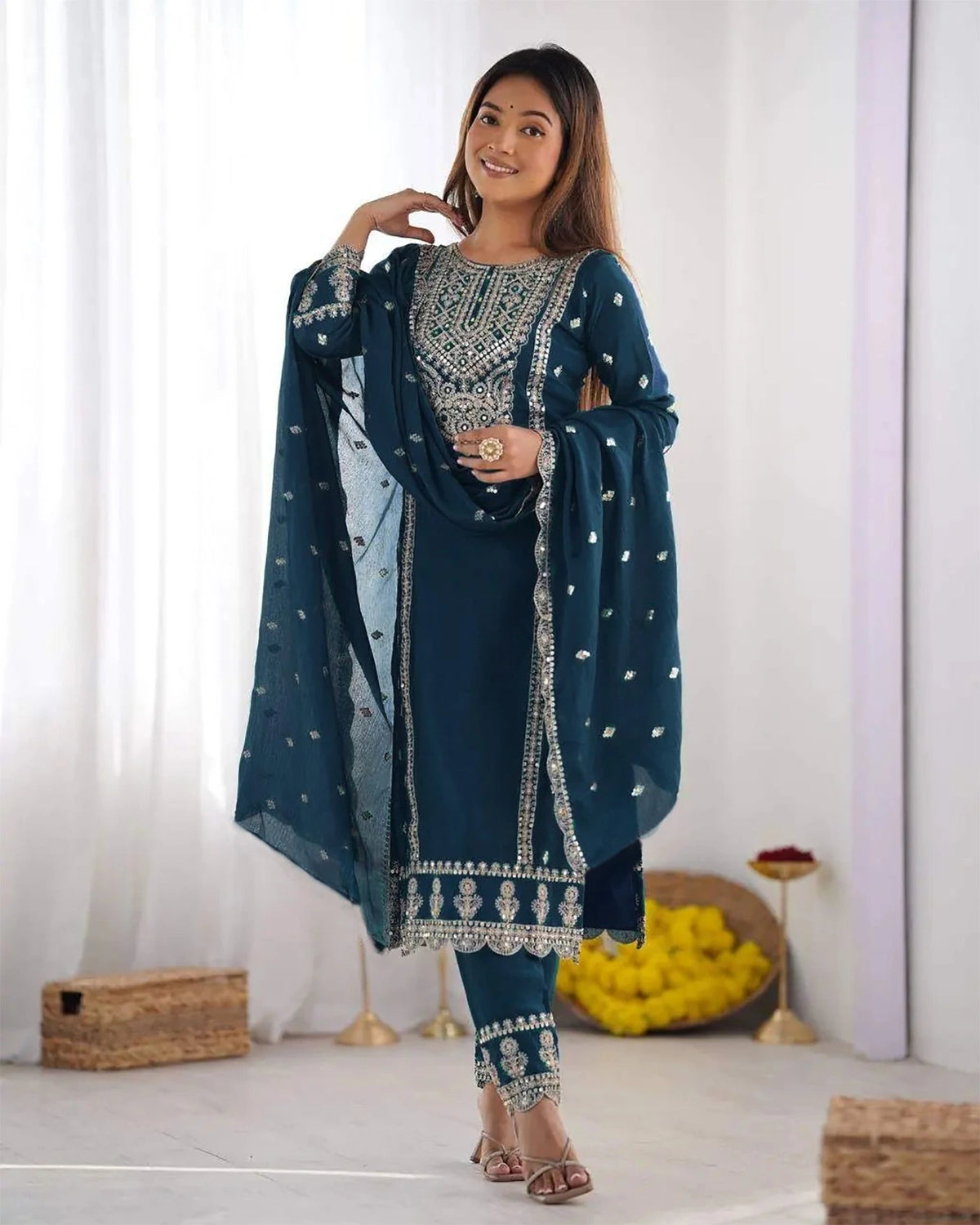 Woman wearing a traditional outfit with a blue and silver design in a minimalistic setting.