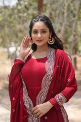 Woman in a red traditional outfit with intricate patterns, waving outdoors.