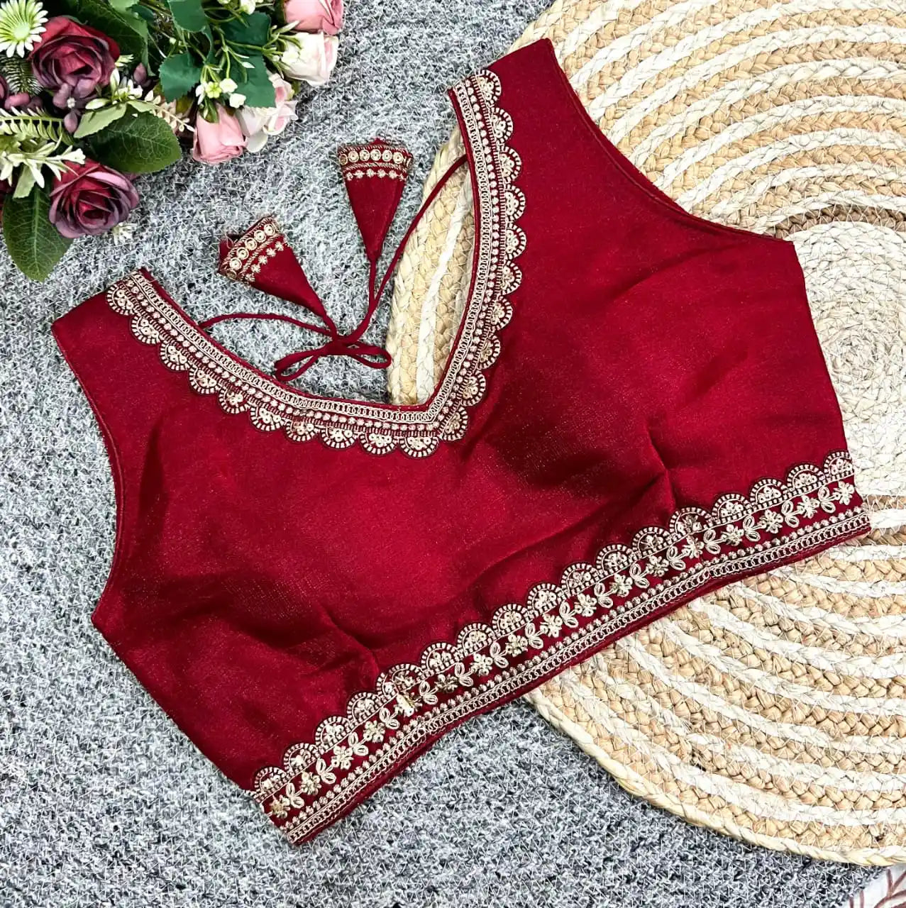 Red blouse with gold embroidery on a textured surface with flowers and a woven mat.