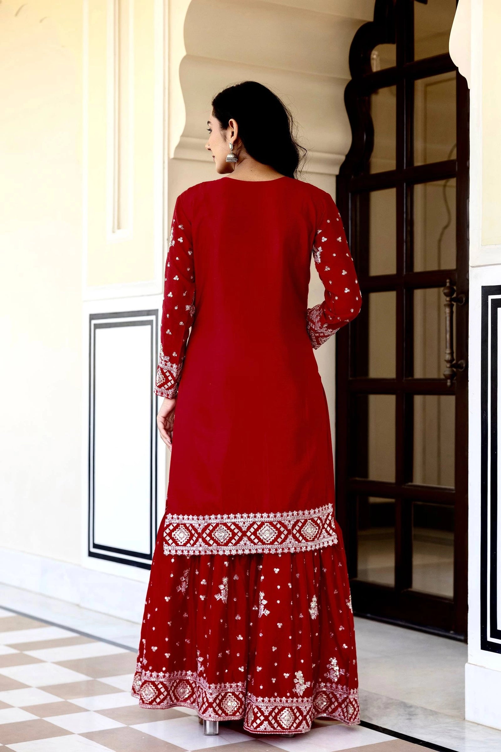Woman wearing a red traditional outfit with white patterns in an indoor setting.