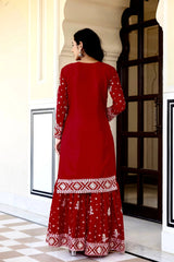 Woman wearing a red traditional outfit with white patterns in an indoor setting.