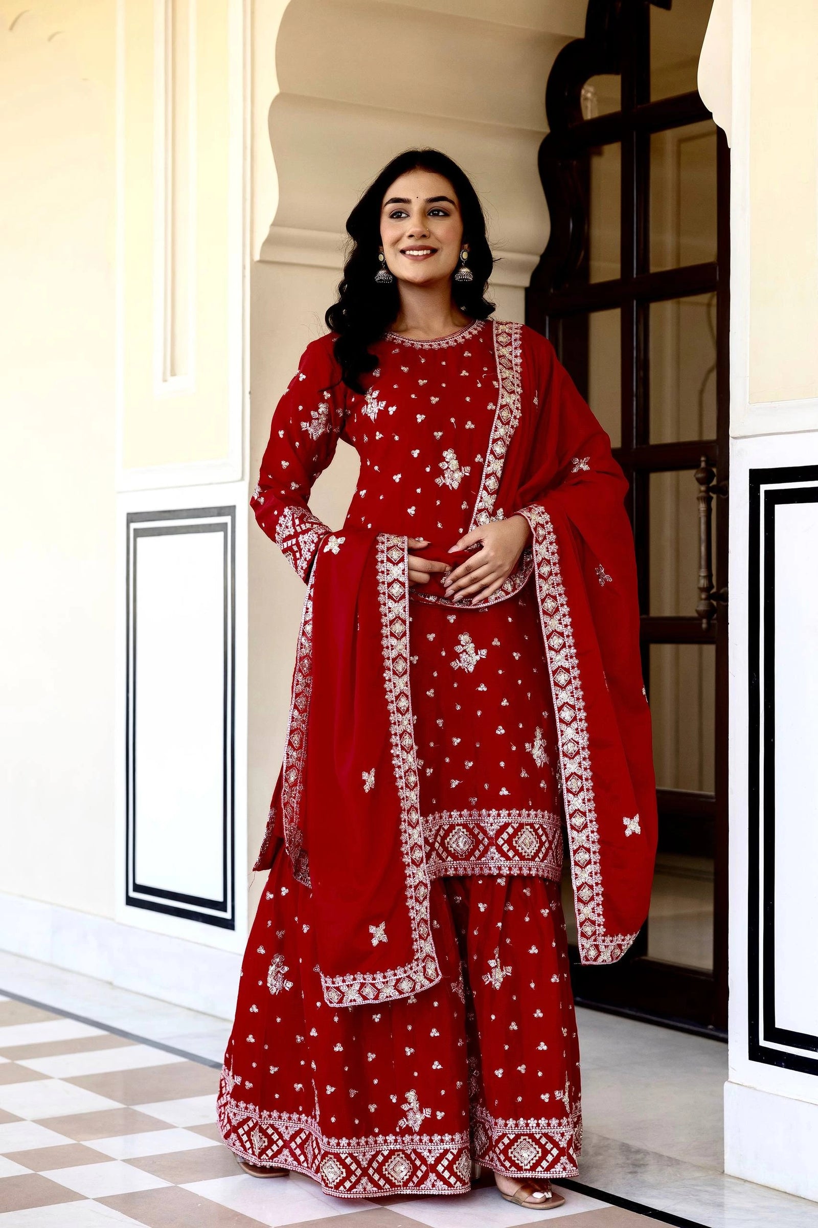 Woman in a red traditional outfit with white patterns standing in a doorway.