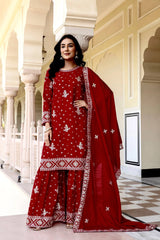 Woman in a red traditional outfit with white patterns standing in an elegant hallway.