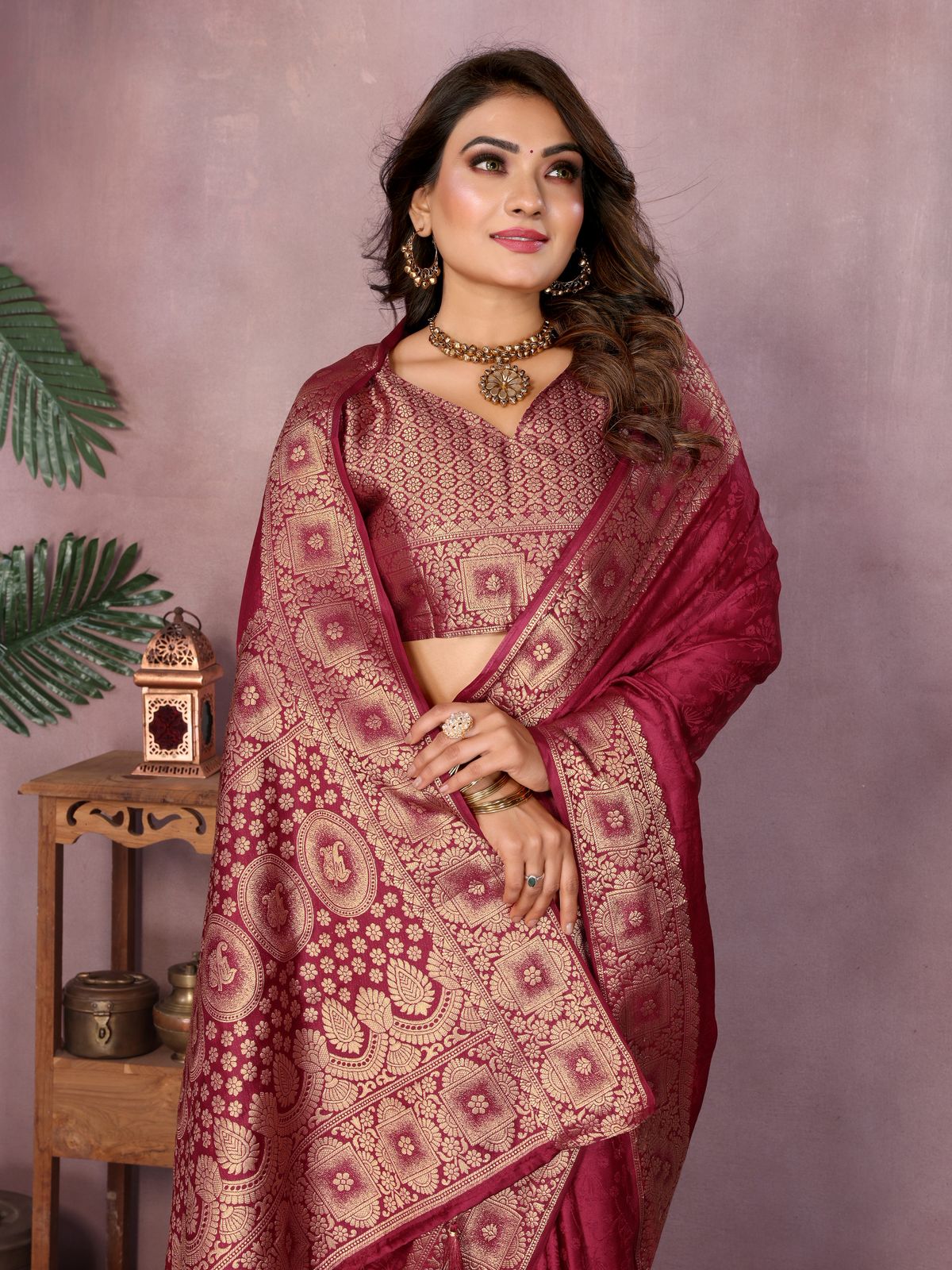 Woman wearing a maroon saree with intricate patterns against a pink background