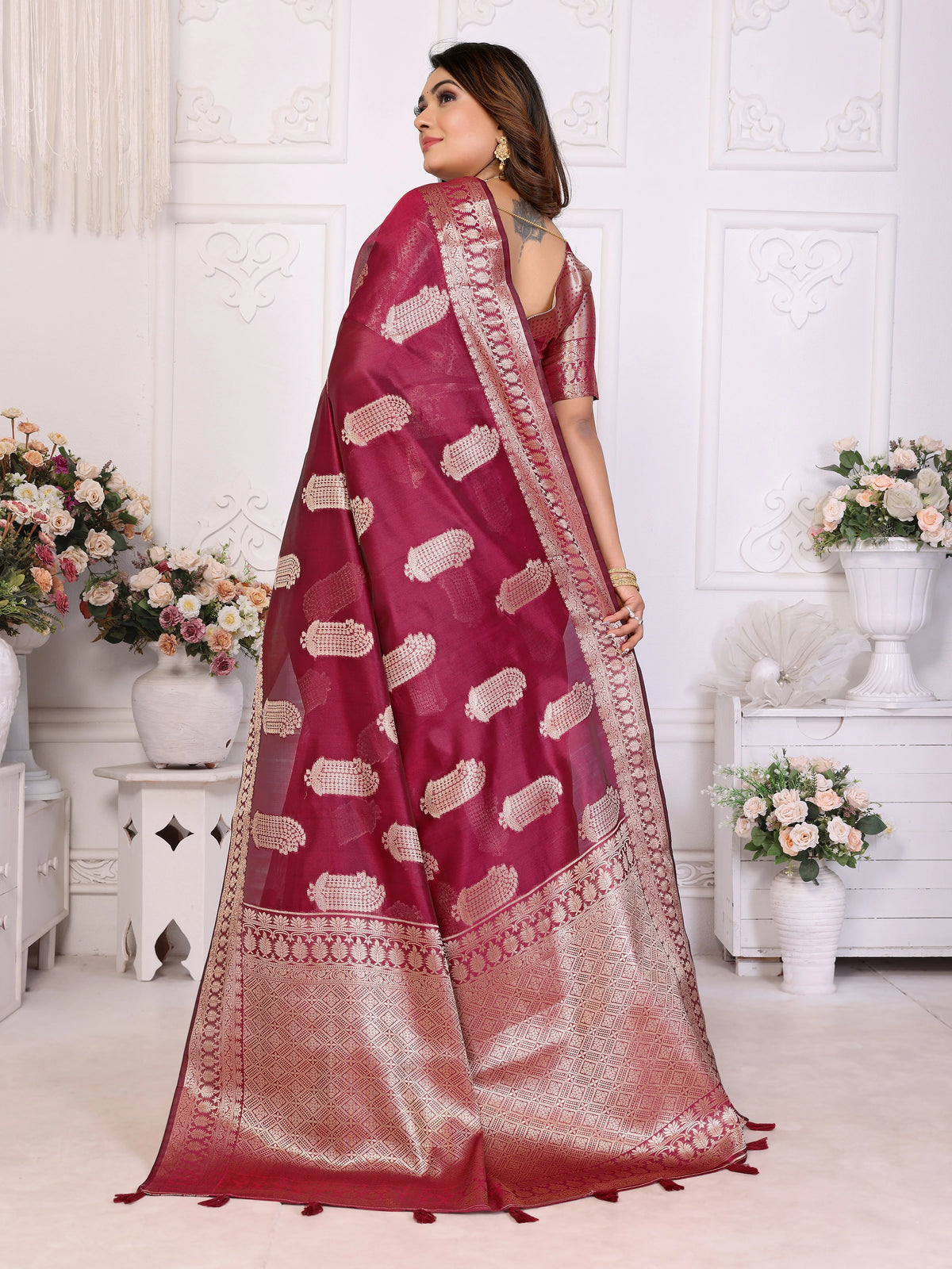 Woman wearing a pink saree with white patterns in a decorated room.