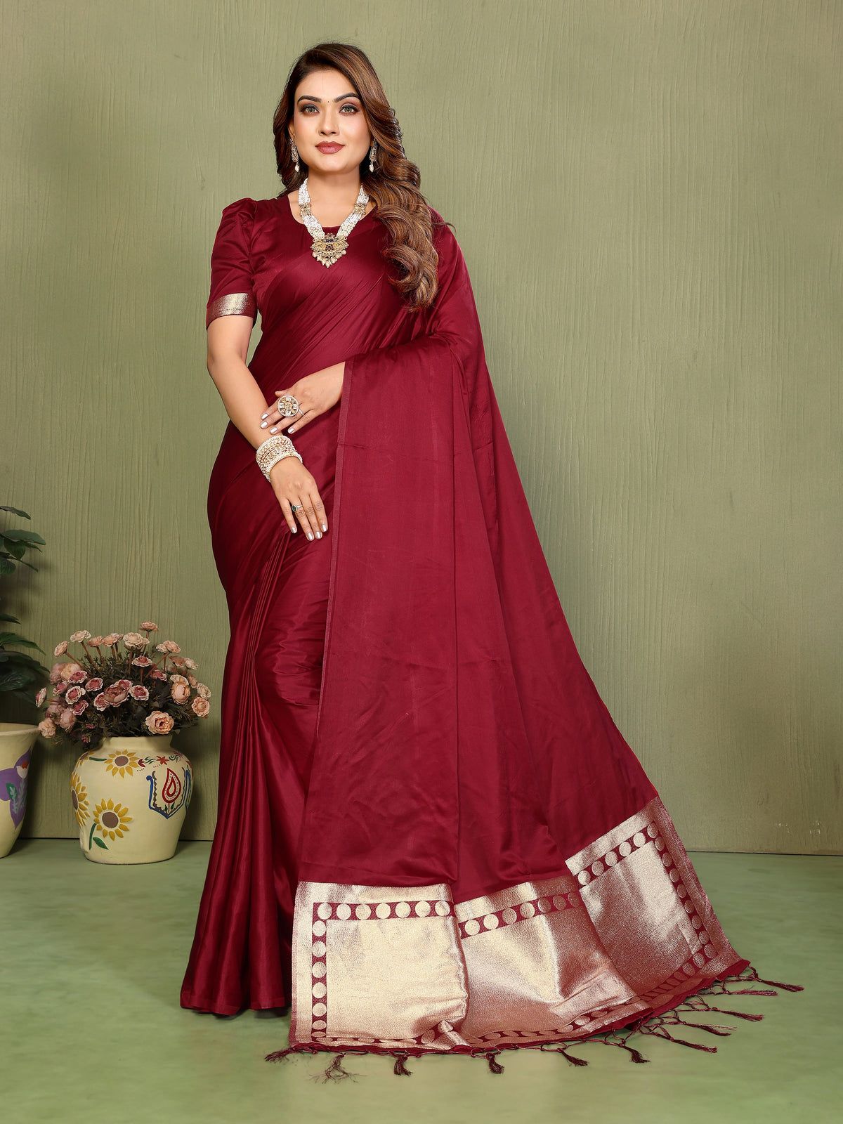 Woman wearing a maroon saree with a white border against a green background