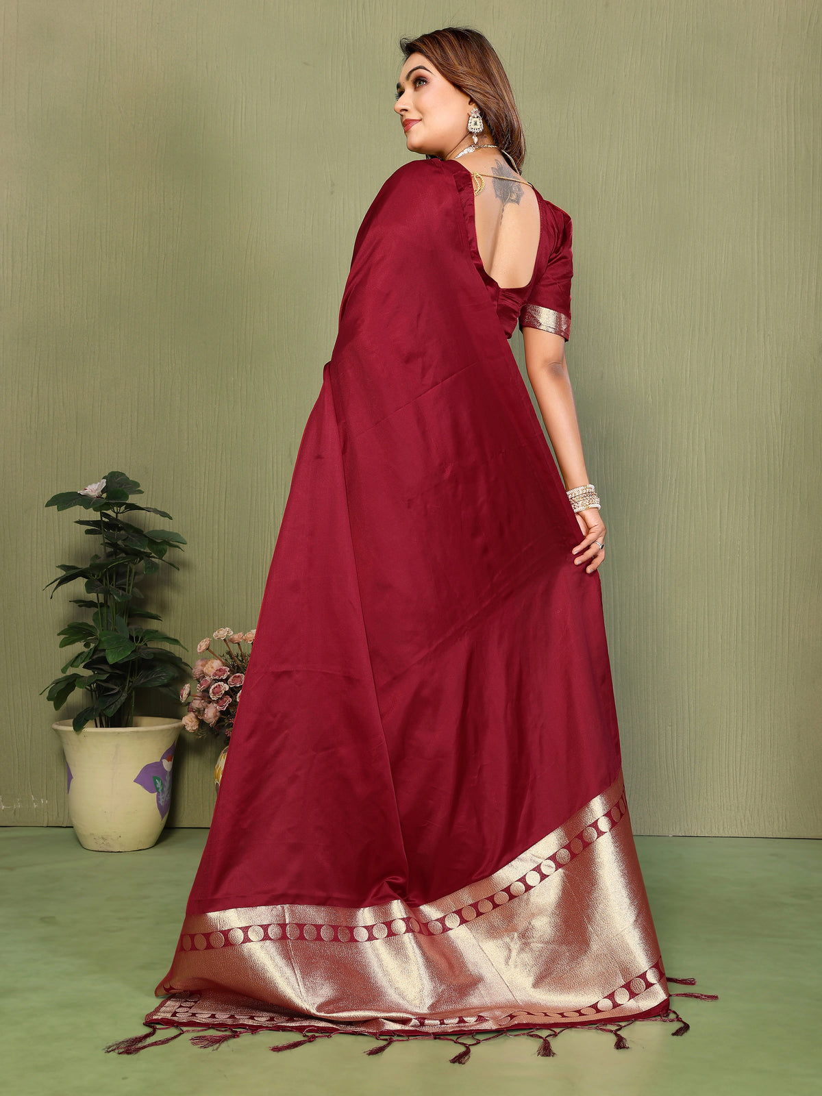 Woman wearing a maroon saree with a gold border against a green background