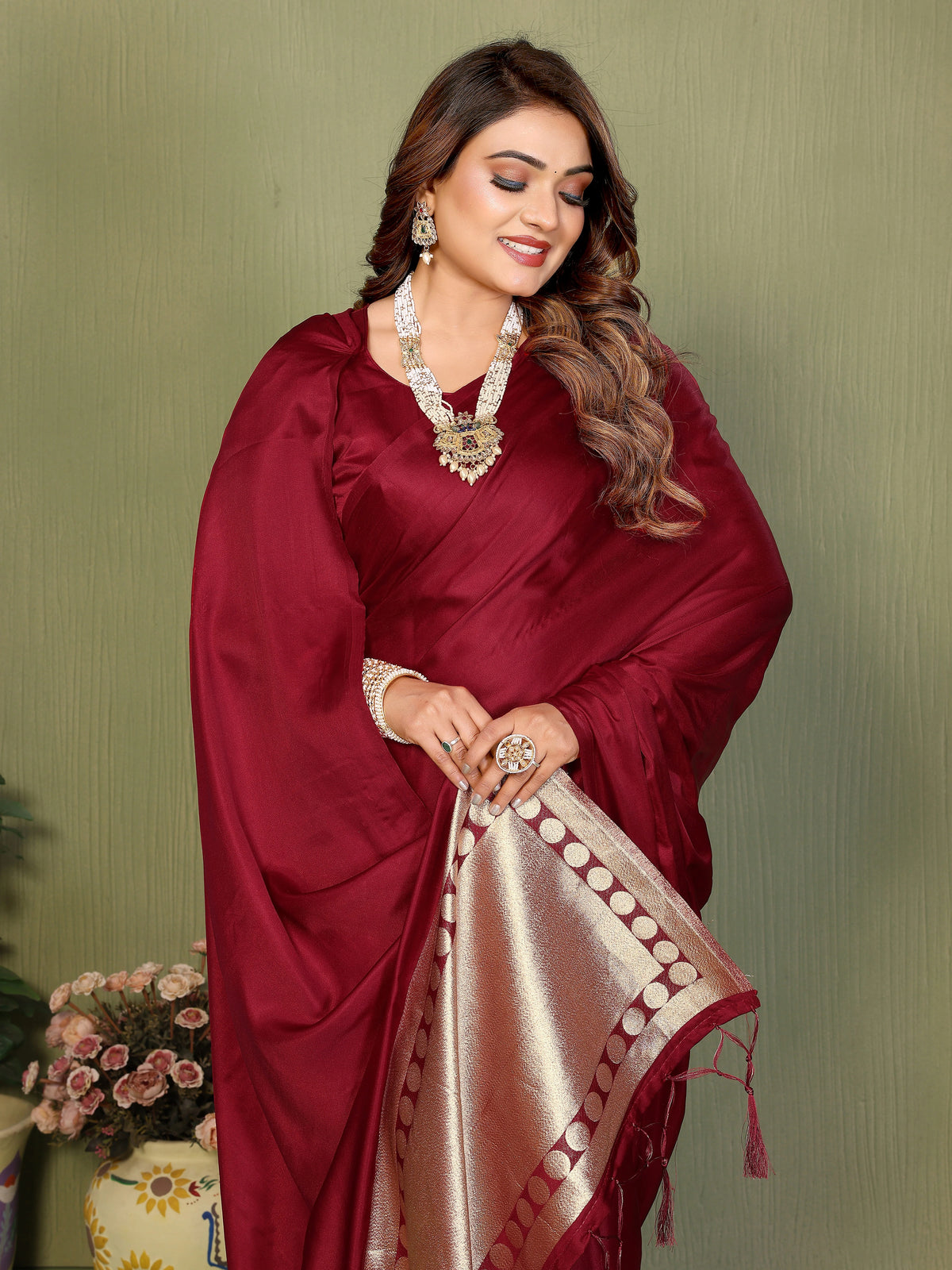 Woman wearing a maroon saree with a gold border against a green background