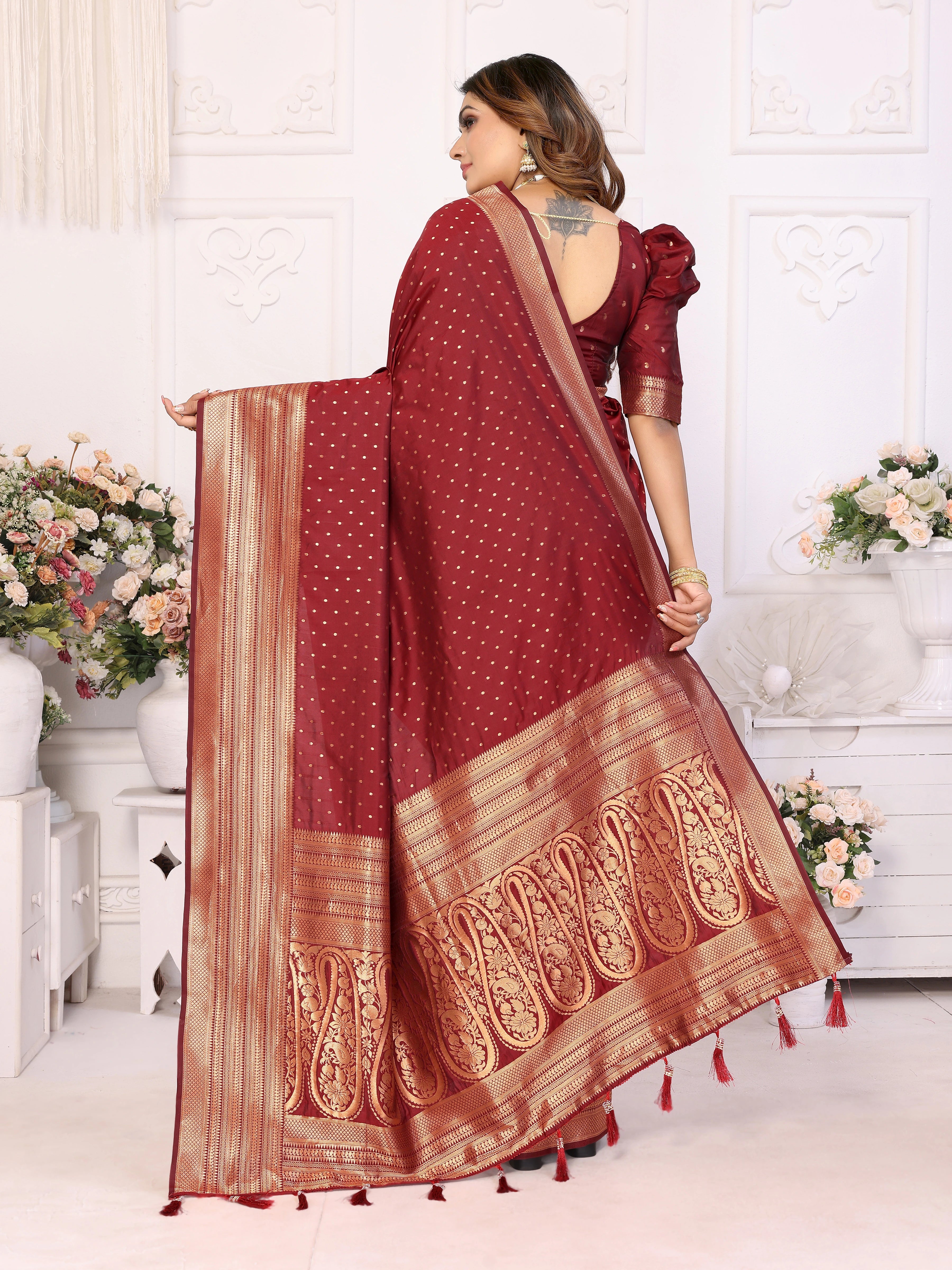 Woman wearing a red saree with gold patterns in a decorated room.