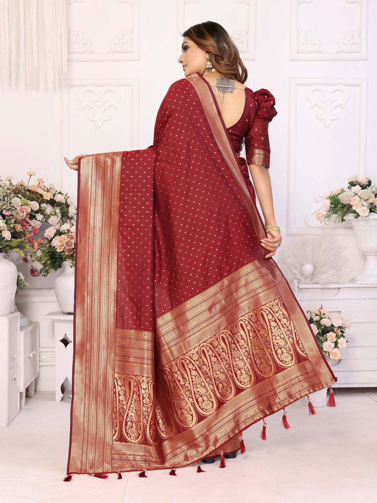 Woman wearing a red saree with gold patterns in a decorated room.