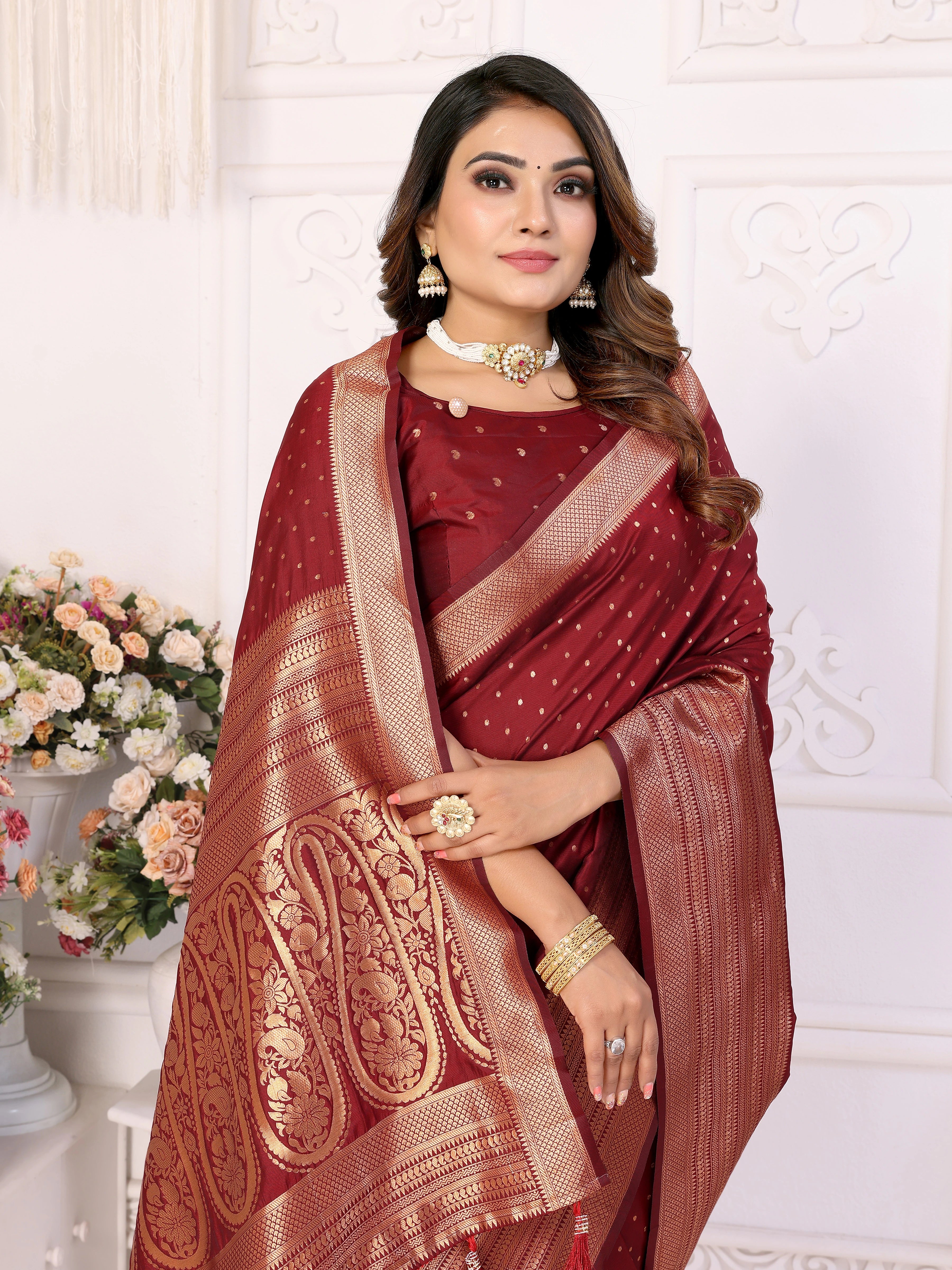 Woman wearing a maroon saree with gold patterns against a white decorative wall.