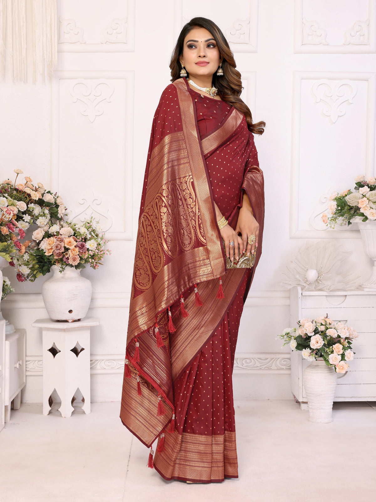 Woman wearing a traditional maroon saree with gold patterns in a decorated room.
