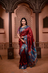 Woman in a red saree with blue patterns standing in an ornate room.