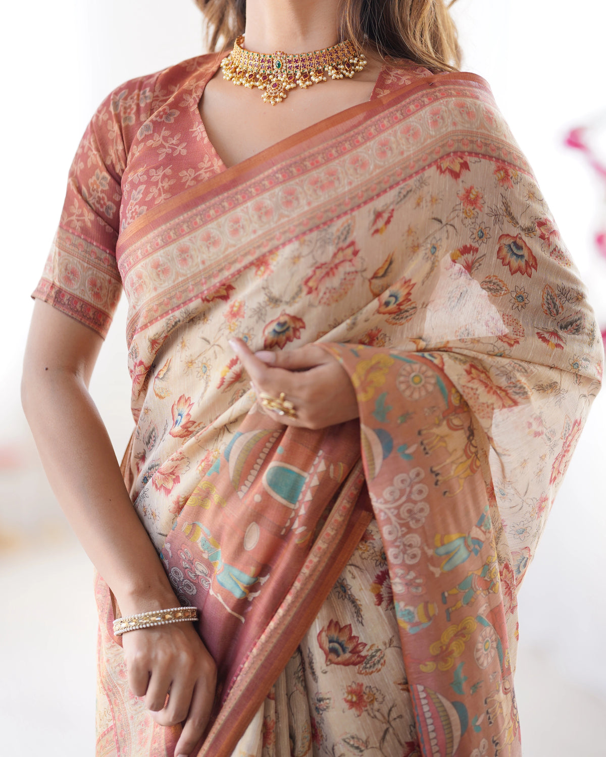 Woman wearing a floral saree with a gold necklace and bracelet on a white background