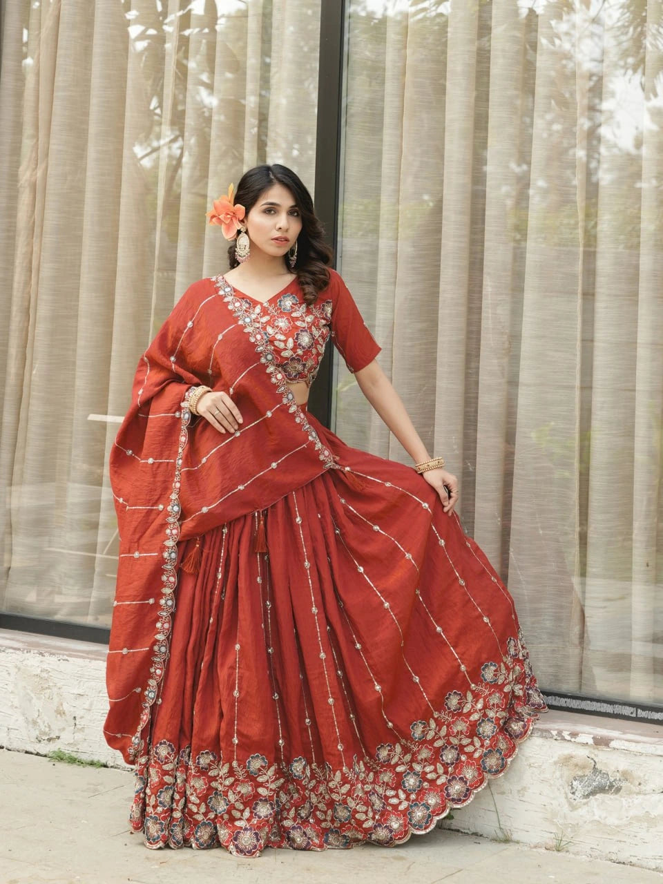 Woman in a red saree with intricate patterns standing against a neutral background