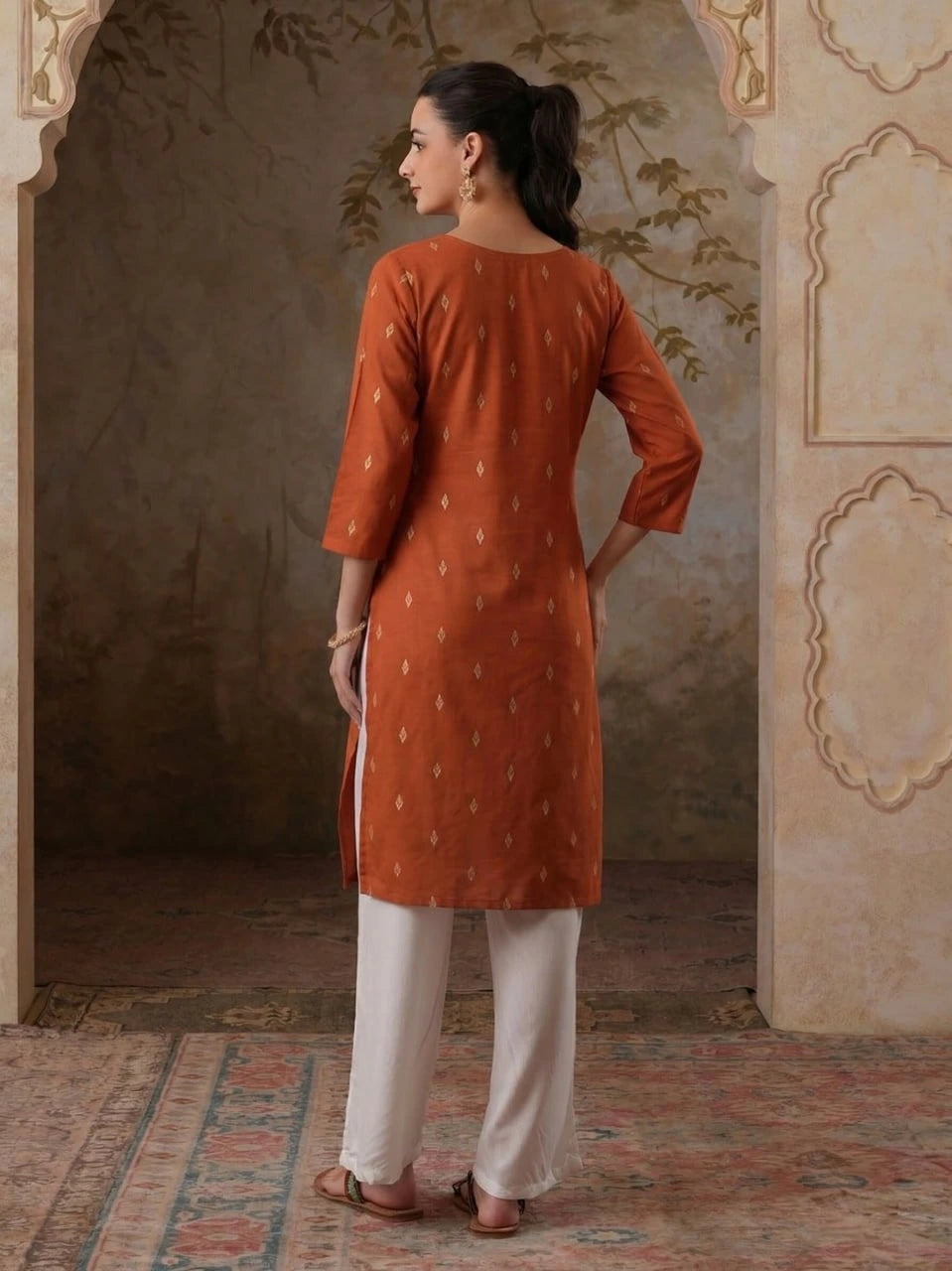 Woman wearing an orange kurta with white pants in a decorative interior setting