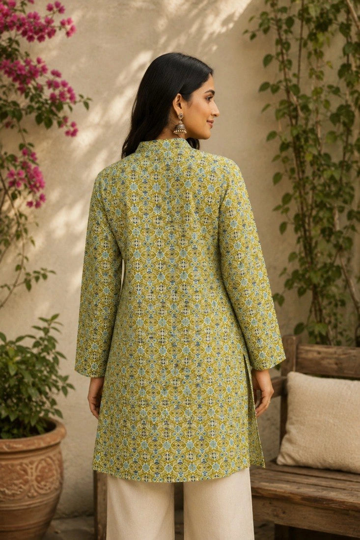 Woman wearing a green patterned kurta standing outdoors with plants and a wall in the background