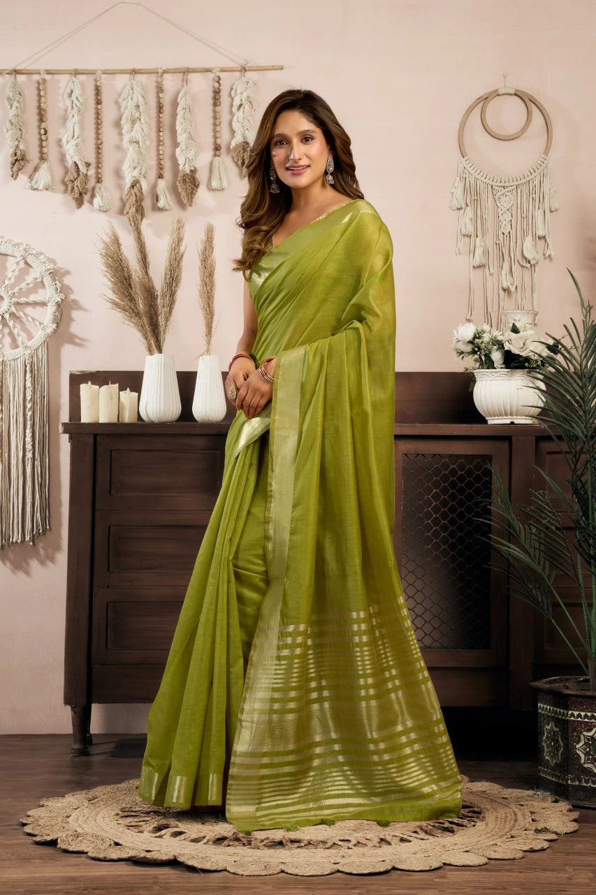 Woman in a green saree standing in a room with decorative elements.