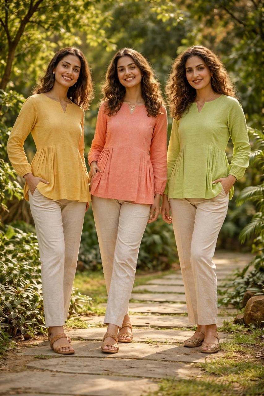 Three women standing outdoors on a path with greenery, wearing colorful tops and beige pants.
