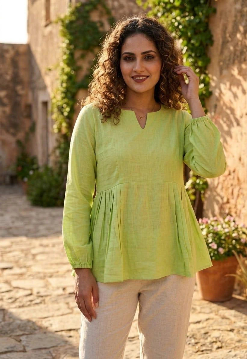 Woman wearing a light green blouse standing outdoors with stone walls and plants in the background