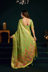 Woman in a green saree with floral patterns standing on steps against a dark background