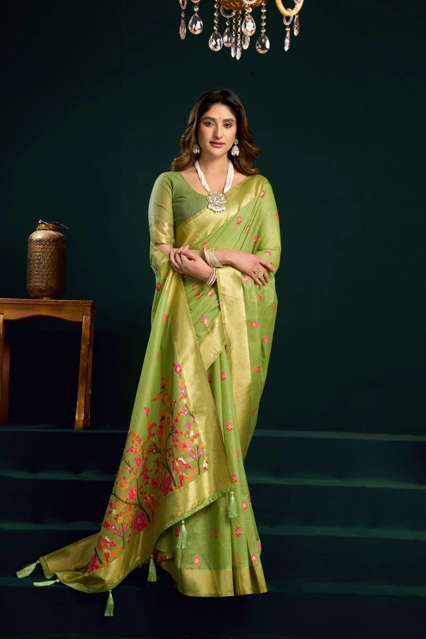Woman in a green saree with floral patterns standing against a dark background